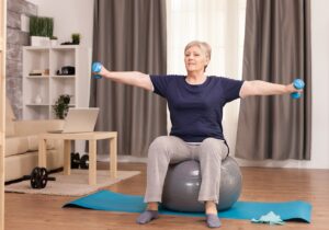 Old person pensioner online internet exercise training at home sport activity with dumbbell, resistance band, swiss ball at elderly retirement age