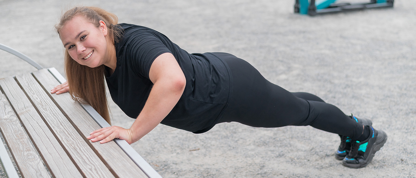 Fat young woman push up from the bench outdoors. A chubby smiling girl warms up before jogging. Sports for weight loss.
